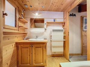 Une salle de bain aux murs lambrés, équipée d’un lavabo, d’un miroir et d’un radiateur.