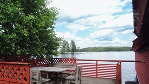 A wooden deck with a table and benches overlooking a lake, surrounded by a red fence and a tree.