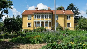 A yellow building with a red-tiled roof, surrounded by a garden with various plants and flowers.
