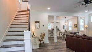 Un vaste espace de vie comprenant un escalier, un canapé en cuir marron et, au fond, un coin repas.