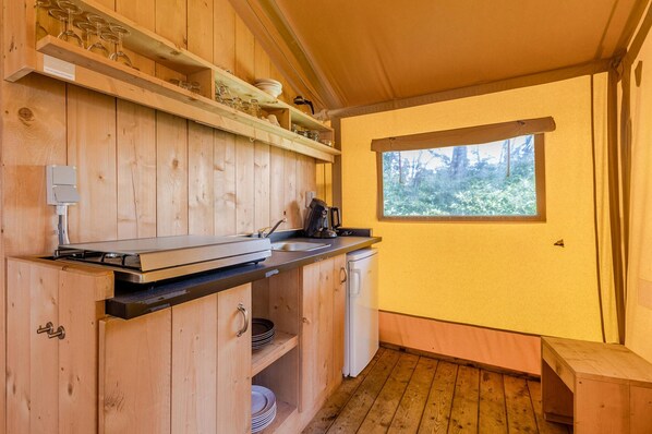 Cozinha compacta com armários de madeira, fogão embutido, pia e janela com vista para árvores.