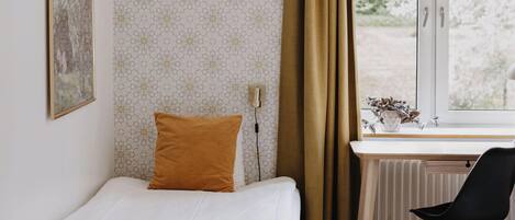 A small, neatly arranged bedroom with a bed, a desk, and a chair.
