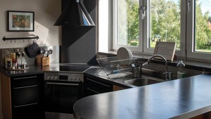 A modern kitchen with a central island, a stove, oven, and a large window providing a view of greenery outside. - Vassbo Logi & Event (Falun)