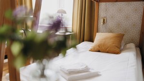 A neatly made bed with a folded white towel, a single yellow pillow, and a patterned wall in the background. - Vassbo Logi & Event (Falun)