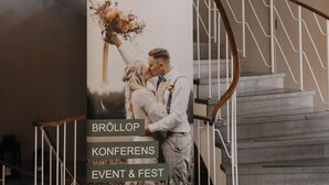 A staircase with a chandelier, a banner advertising an event, and a wooden handrail. - Vassbo Logi & Event (Falun)