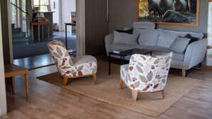 A living room with a grey sofa, two patterned armchairs, a coffee table, and a large painting of sheep. - Vassbo Logi & Event (Falun)