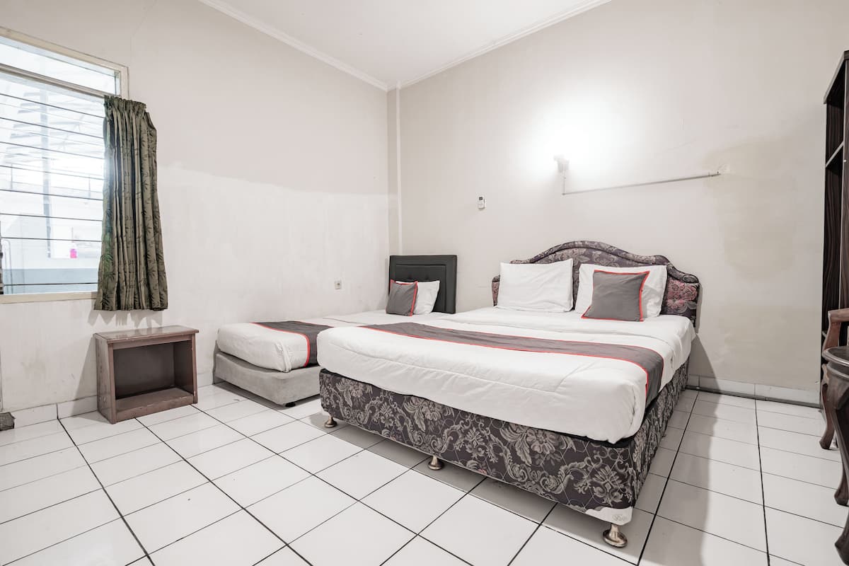 A bedroom with a large bed, a smaller bed, a nightstand, a window with curtains, and a wall-mounted light fixture.