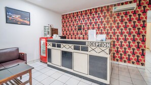 A reception area with a red patterned wall, a reception desk, a Coca-Cola refrigerator, and a framed picture on the wall. - Collection O Hotel Sanira (Bandung)