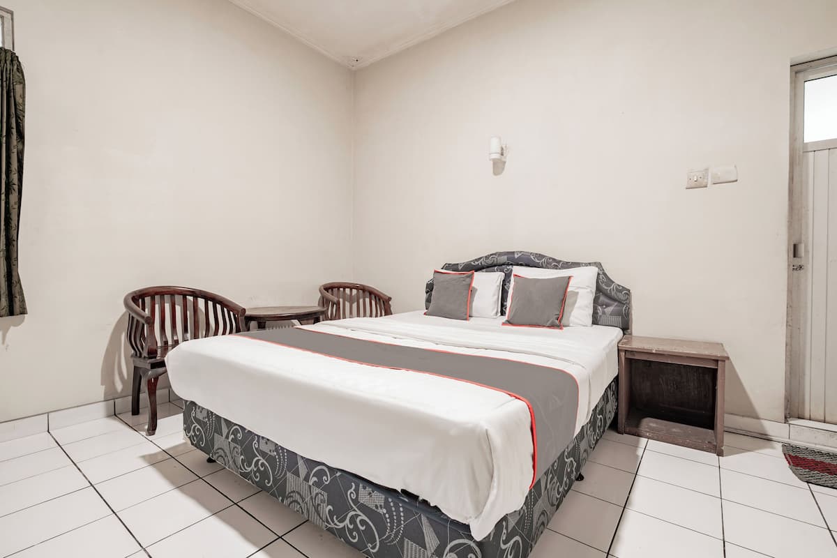 A bedroom with a bed, two chairs, a small table, and a nightstand.