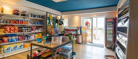 Interior de una tienda de comestibles con estantes llenos de bocadillos, bebidas y artículos para el hogar.