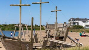 Una playa con estructuras de madera, incluyendo un bote y un tobogán, y un edificio al fondo.
