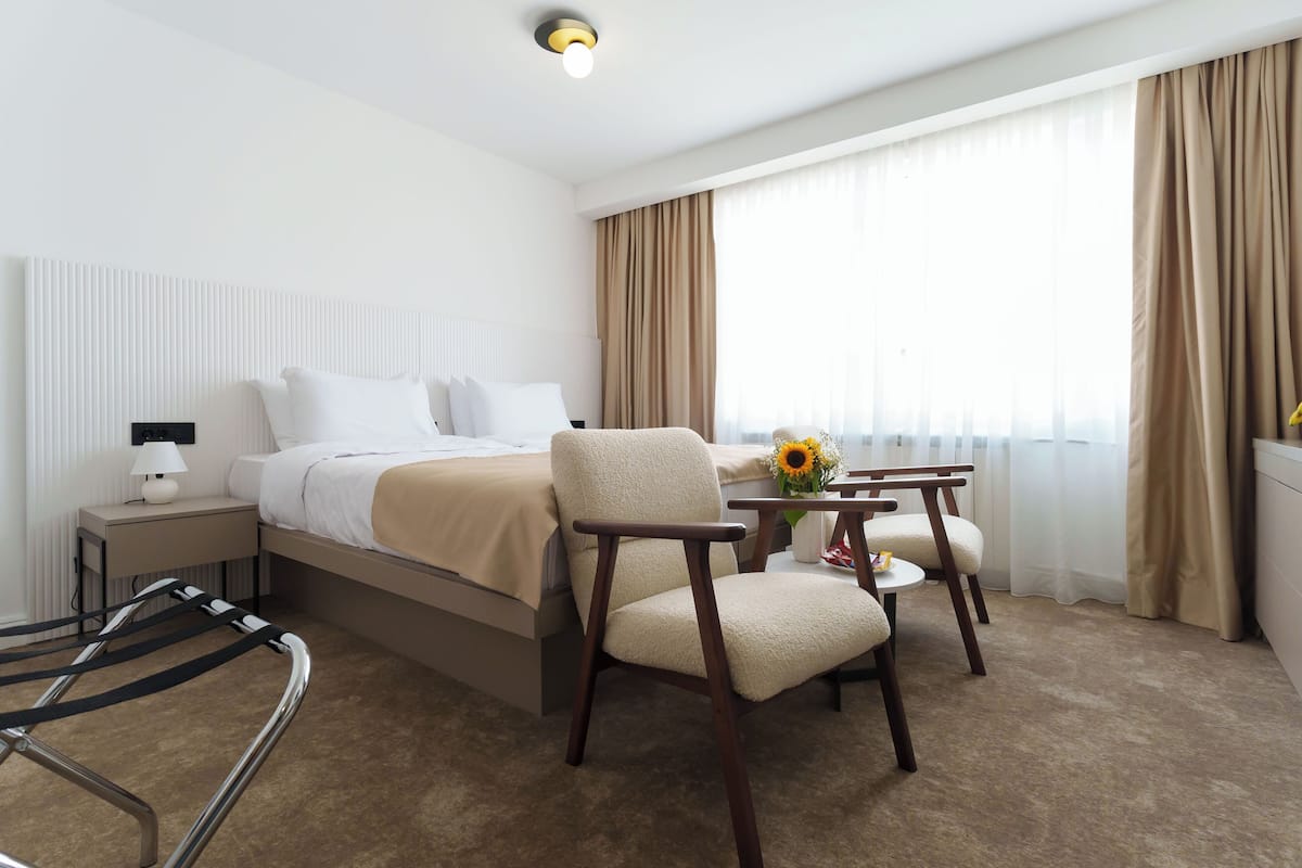 Ein Hotelzimmer mit einem Bett, einem Sessel, einem kleinen Tisch mit Blumenvase und einer Lampe.