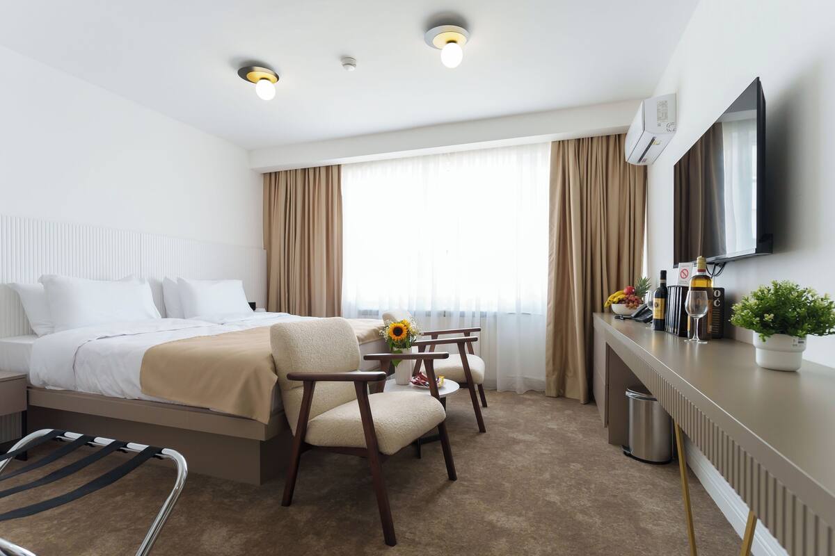 Ein Hotelzimmer mit einem Bett, einem Schreibtisch, einem Stuhl, einem Fernseher und einem fenster mit Vorhängen.