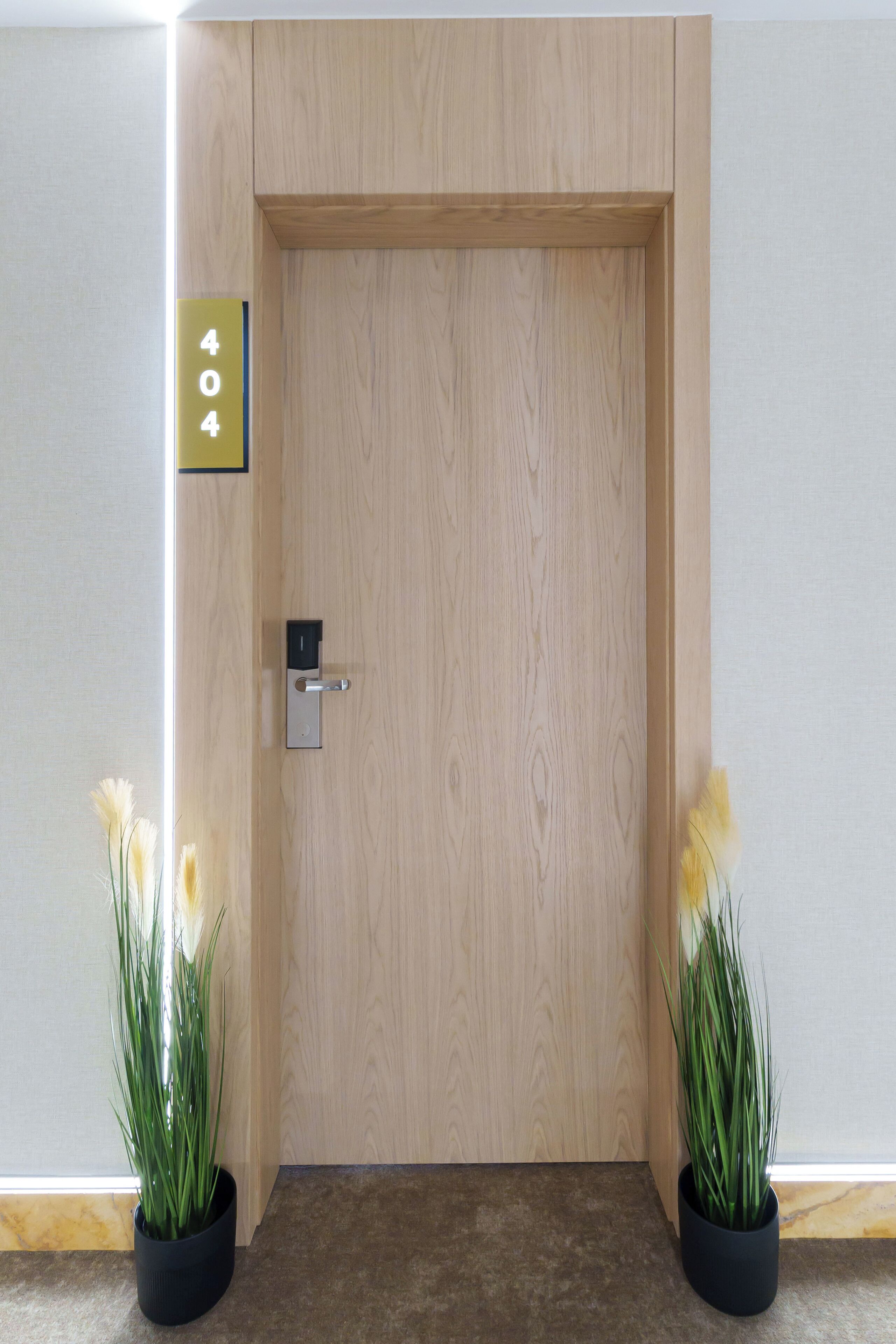 A wooden door with a digital lock and a sign indicating room number 404. There are two potted plants on either side of the door.