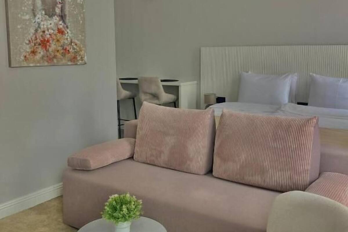 Ein modernes Schlafzimmer mit einem Bett, einem Sofa, einem kleinen runden Tisch mit Pflanze und einem Gemälde an der Wand.