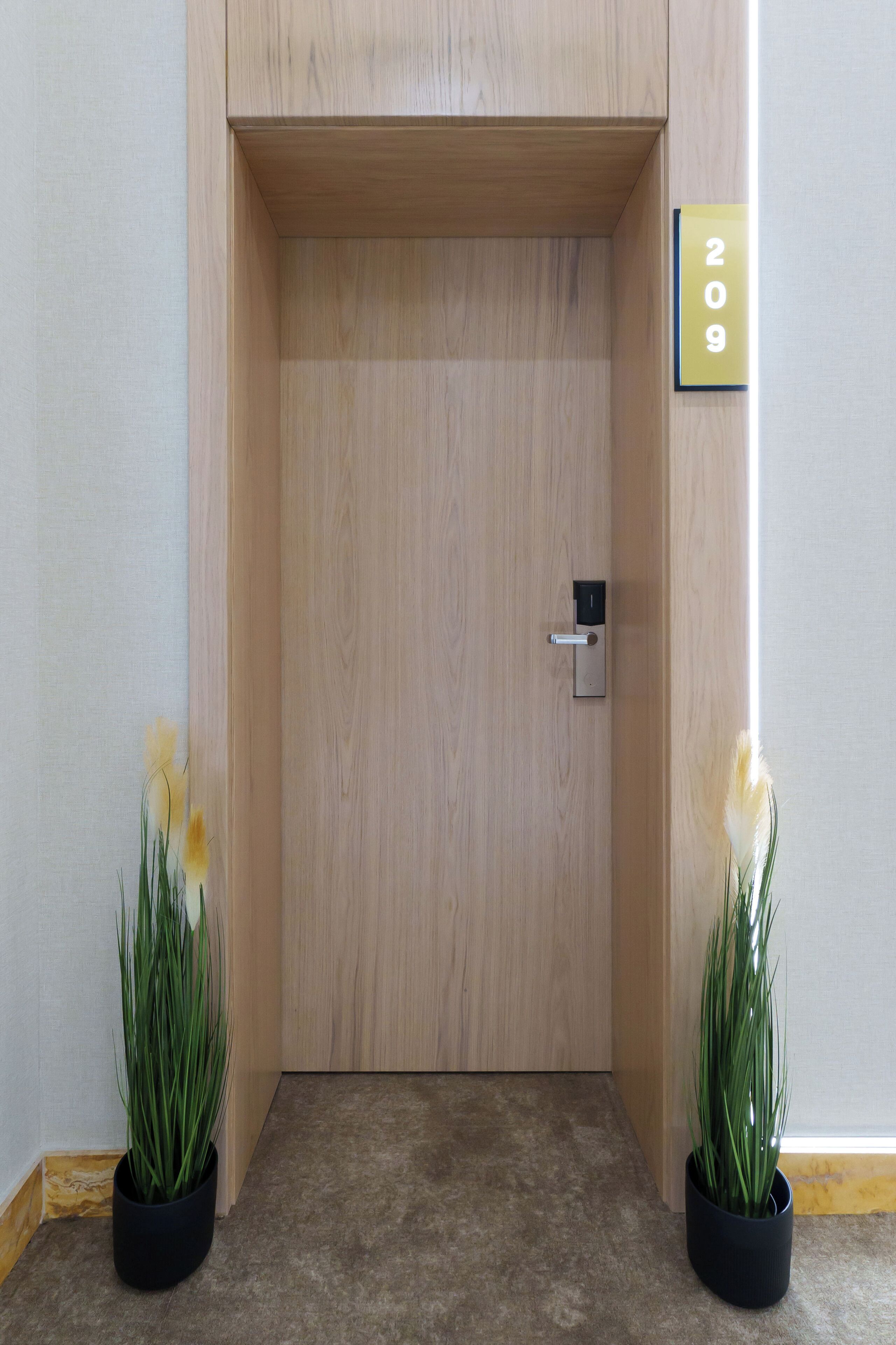 A wooden door with a numeric sign, a keyhole, and two potted plants.