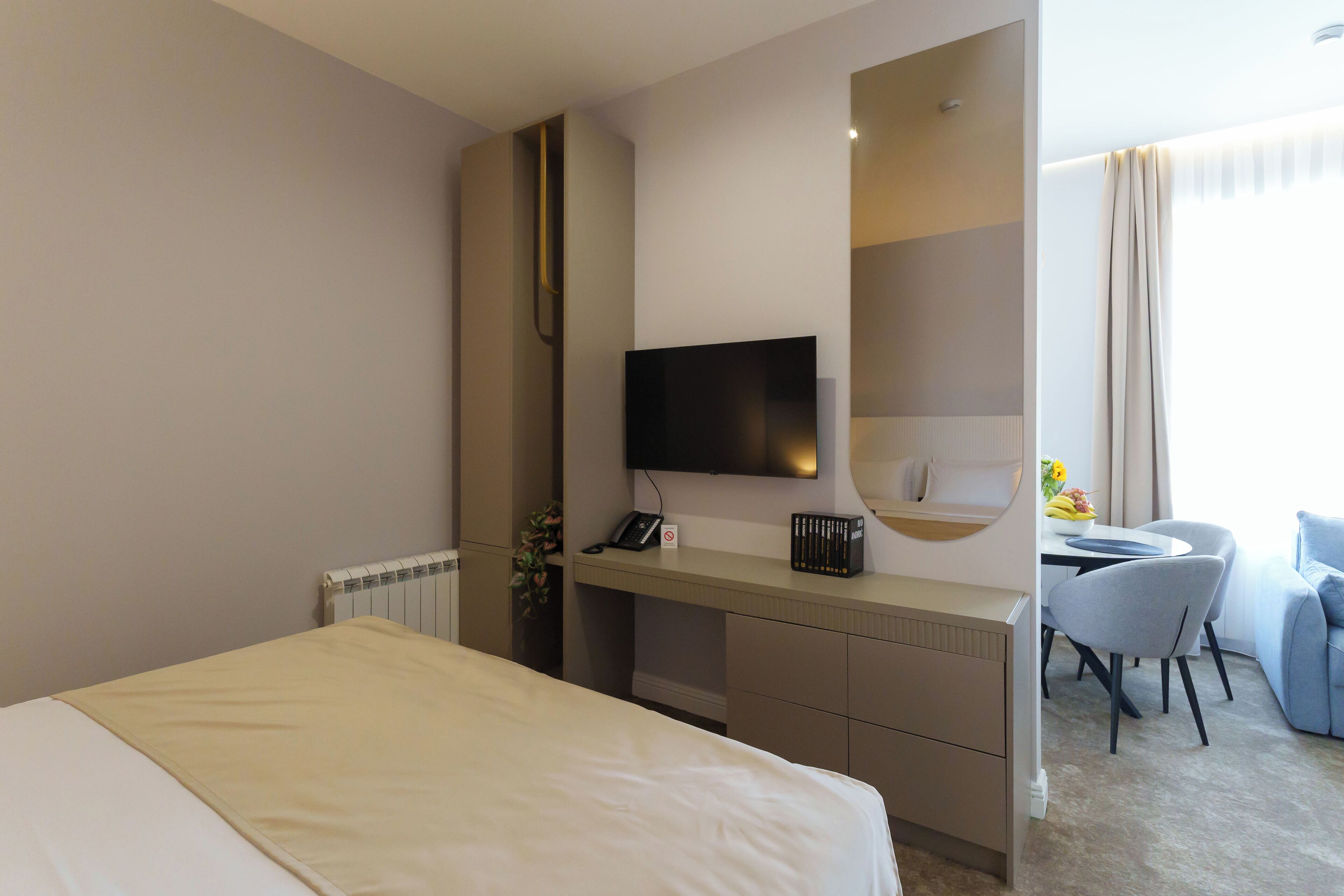 A hotel room with a bed, a desk with a flat-screen TV, a chair, and a small dining table.
