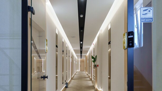 Un couloir d’hôtel avec des portes en verre, un sol recouvert de moquette et un panneau indiquant la présence de caméras de surveillance.
