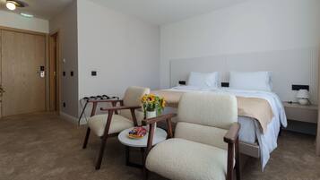 A hotel room with a bed, two armchairs, a small table with a vase of flowers, and a nightstand with a lamp.
