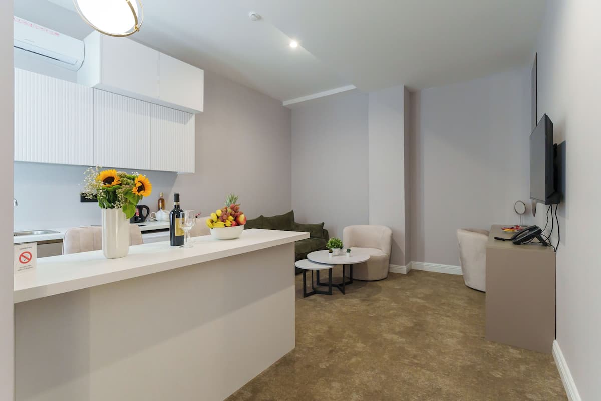 Ein modernes Wohnzimmer mit Küchenbereich, einem runden Couchtisch, einer Couch und einem an der Wand befestigten Fernseher.