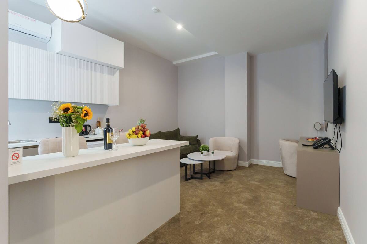 A modern living room with a kitchen area, a round coffee table, a sofa, and a TV mounted on the wall.