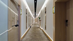 Un long couloir étroit, typique des hôtels, avec des portes des deux côtés, des panneaux numérotés au-dessus de chaque porte et un sol recouvert de moquette.