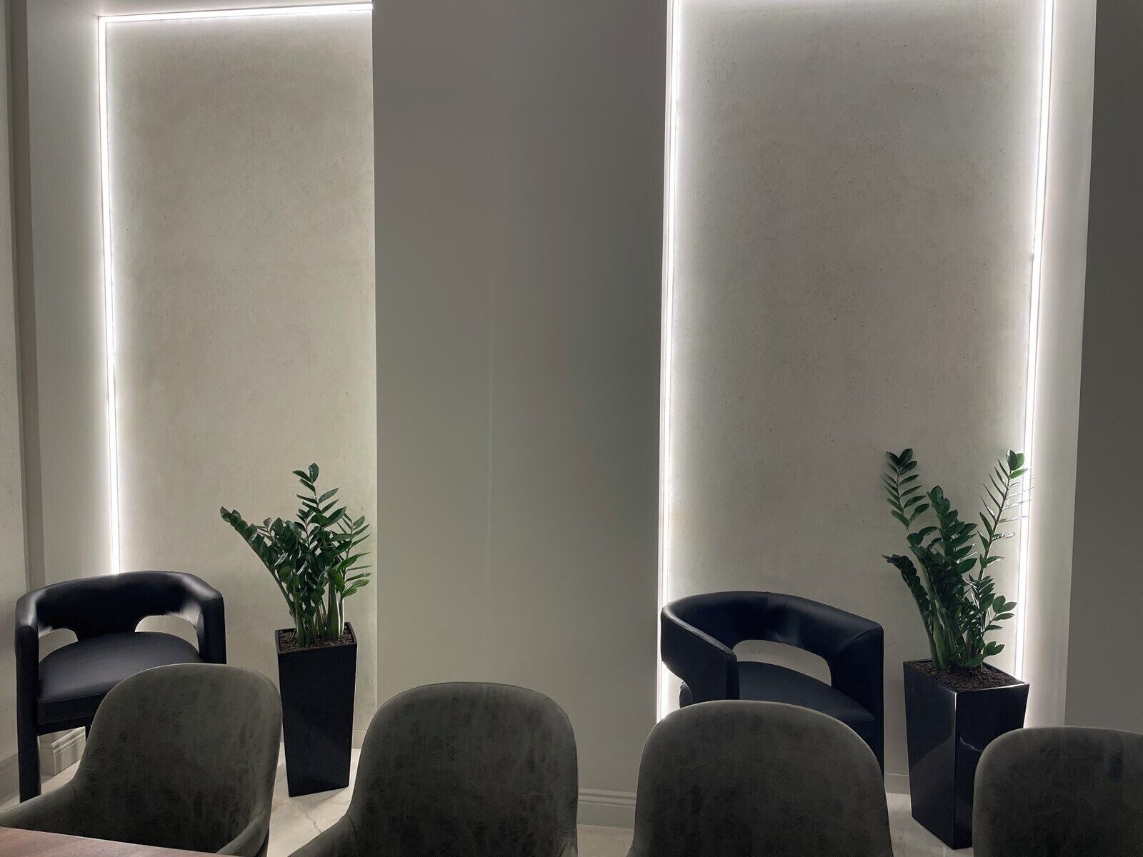 A modern waiting area with two black chairs, a grey sofa, and two potted plants.