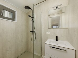 A modern bathroom with a glass shower enclosure, a white sink, and a mirror above it.