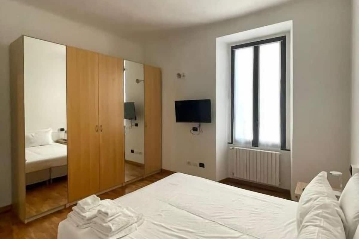 A bedroom with a large bed, a wardrobe, a television, and a window.