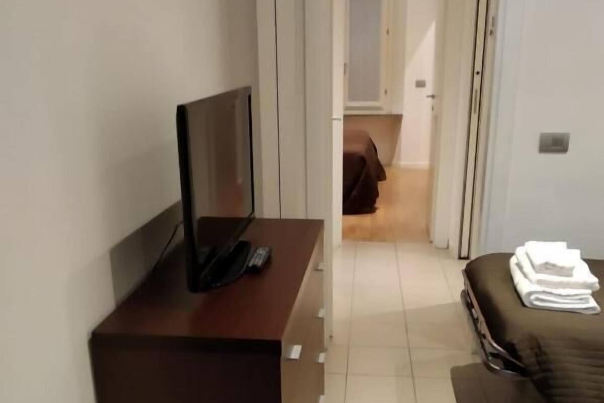 A hotel room with a wooden desk, a television, a bed with a brown cover, and a small table with towels.