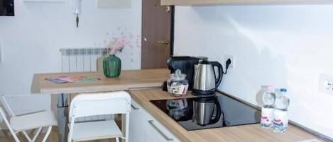 A compact kitchen with a wooden countertop, a coffee maker, and a kettle. There are white cabinets and a small table with chairs.