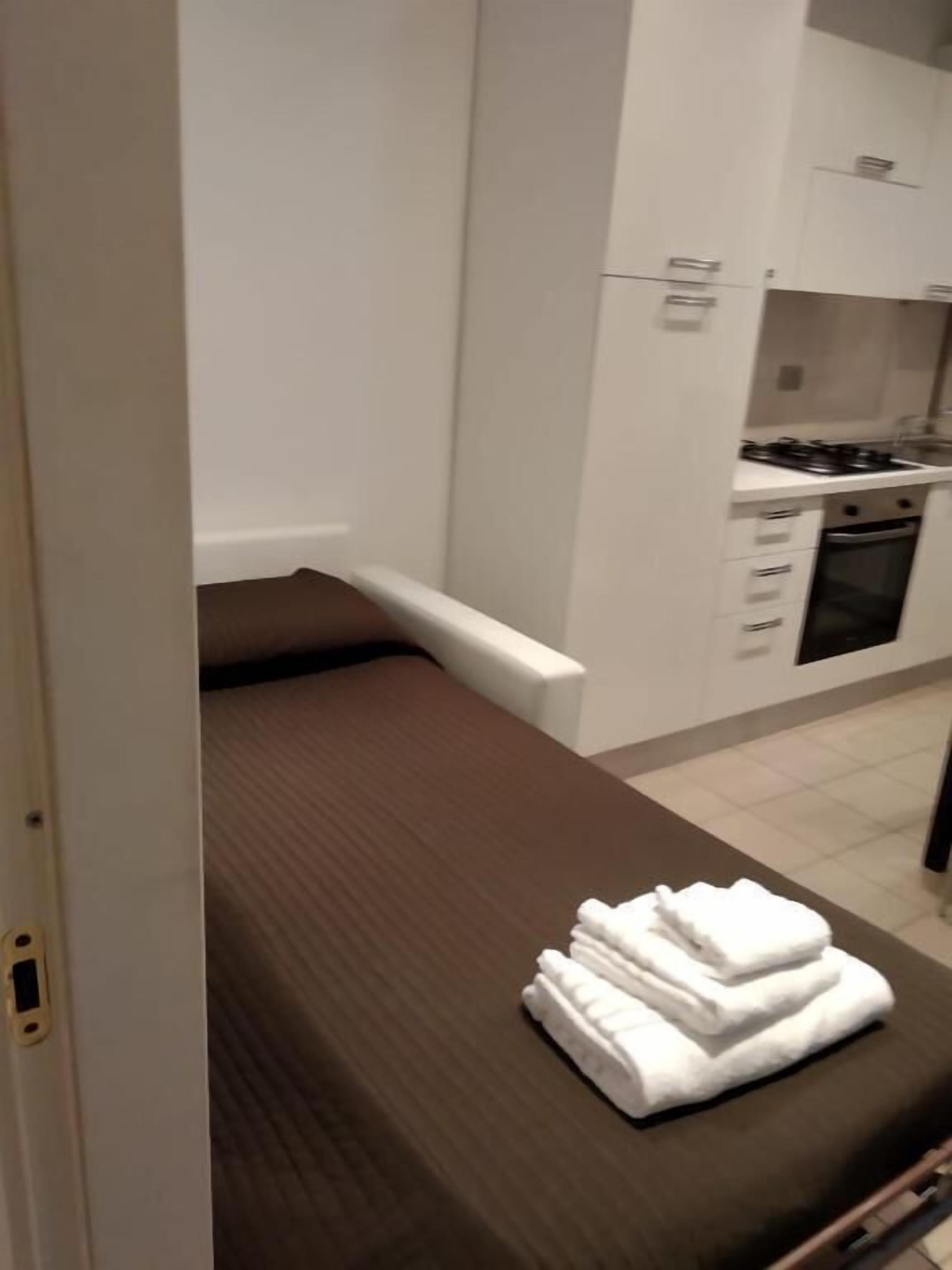 A small, compact room with a single bed, a kitchenette, and a bathroom.