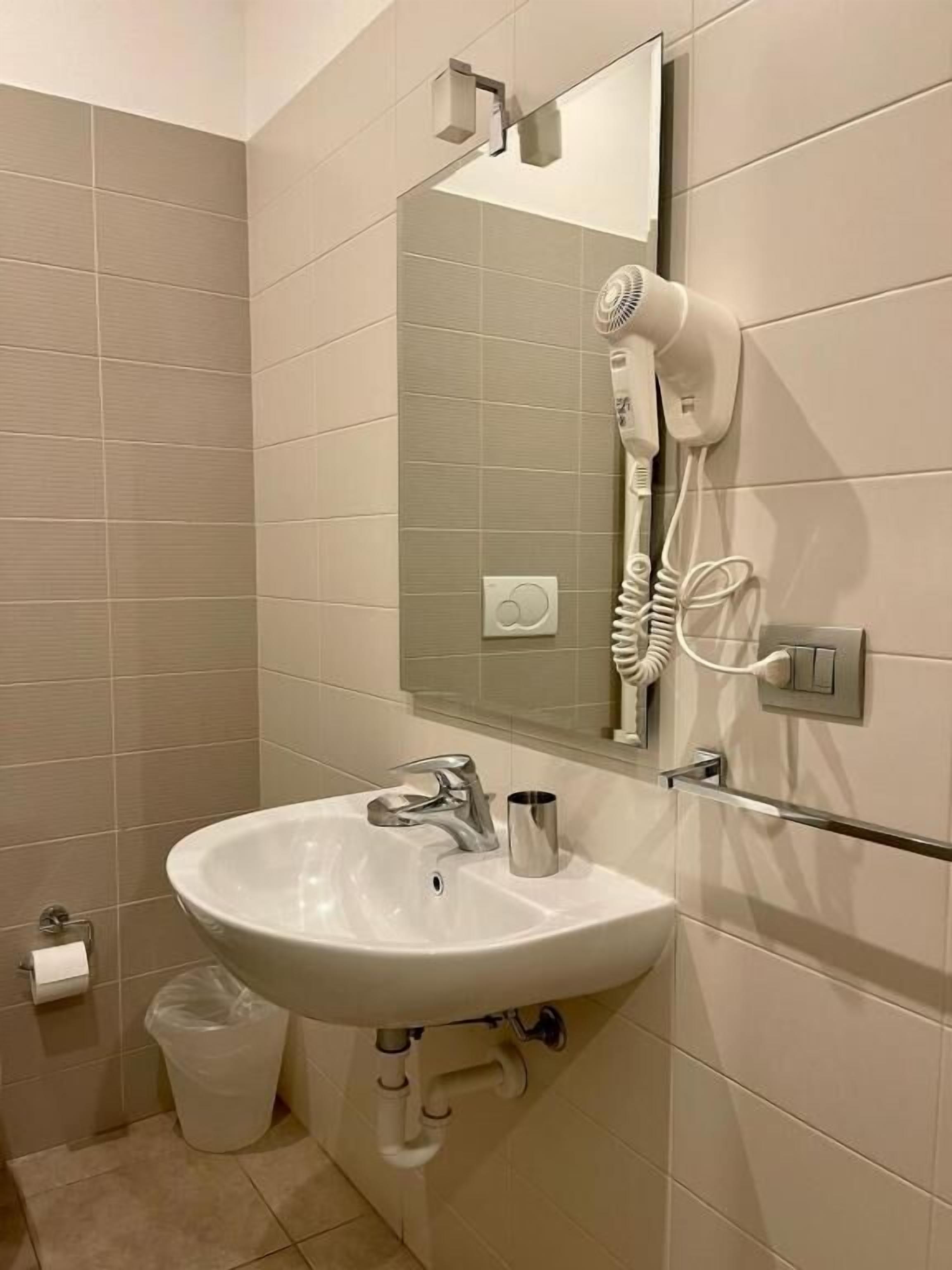 A bathroom with a white sink, a mirror, a hairdryer, and a trash bin.