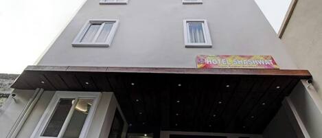 A hotel named HOTEL SHASHWAT with a modern facade, multiple windows, and a covered entrance.