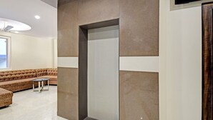 A modern living room with a sectional sofa, a small round table, and a recessed wall feature. - Hotel Shashwat (Gorakhpur)