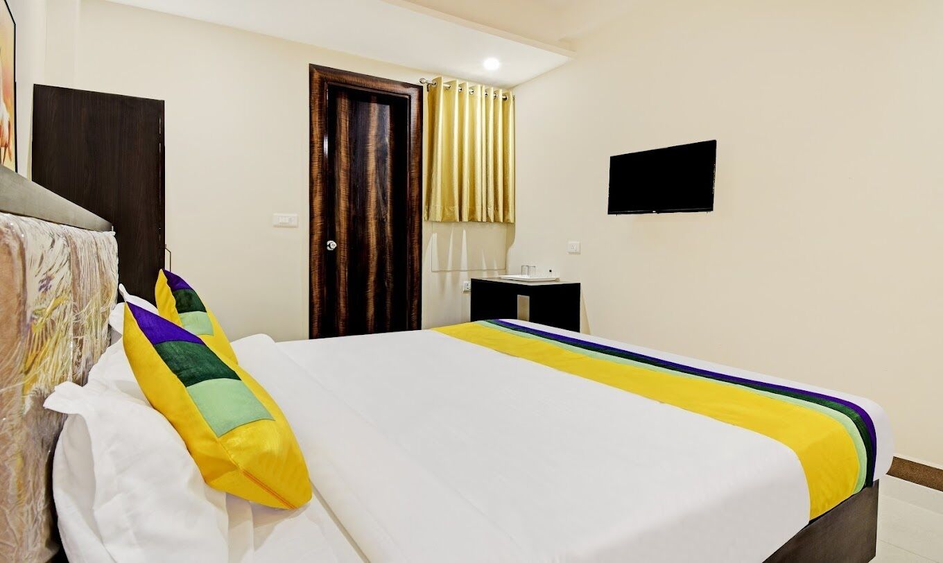 Una habitación de hotel con una cama, una mesita de noche, una puerta y un televisor montado en la pared.