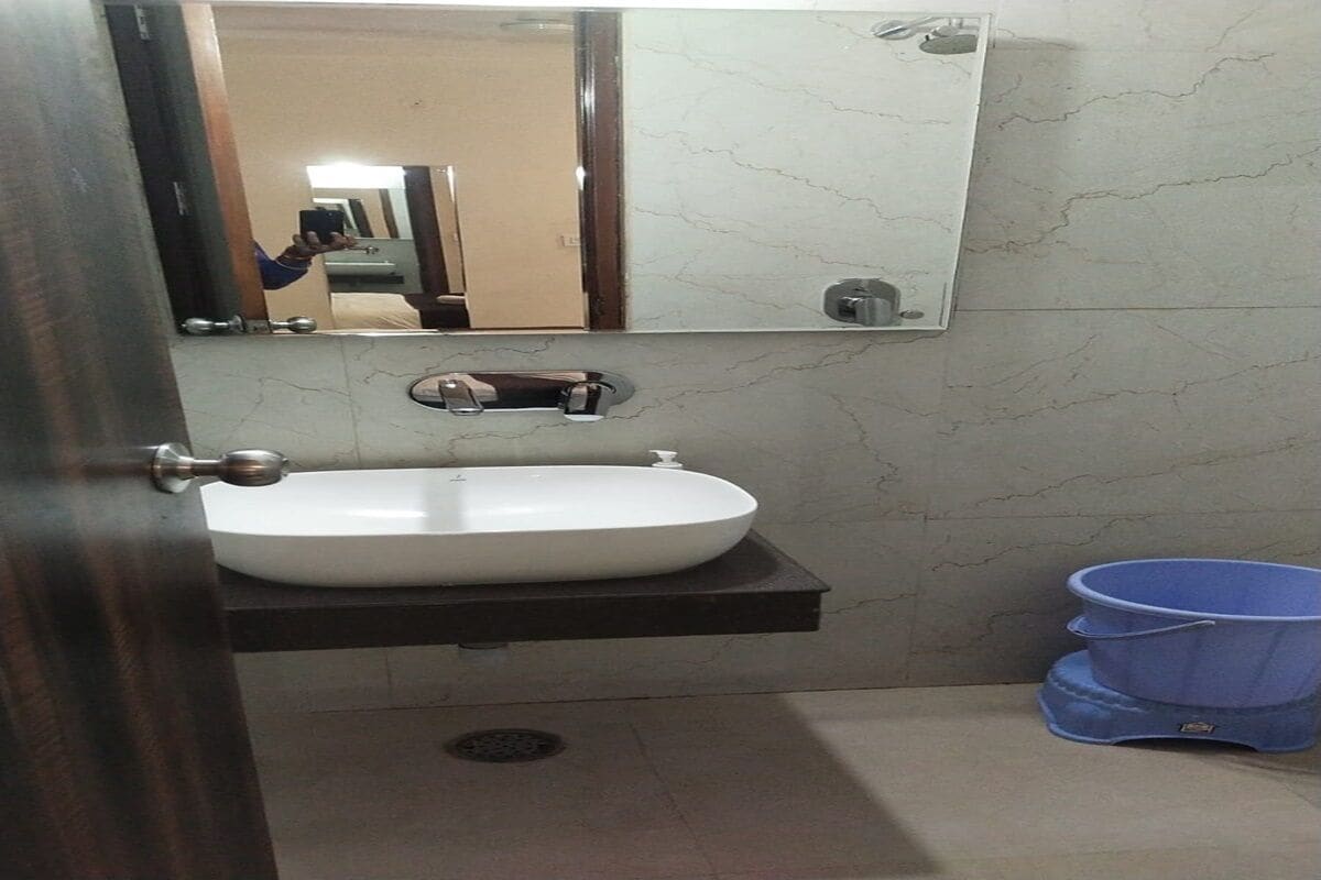 A bathroom with a white sink, a mirror, and a blue bucket.
