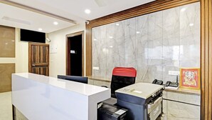 A modern reception area with a marble wall, a reception desk, a chair, a telephone, and a framed picture. - Hotel Shashwat (Gorakhpur)