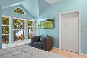 Un dormitorio con una cama grande, una silla, un televisor montado en la pared y una puerta.