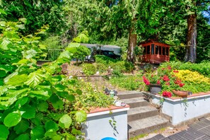 Un jardín con escalones que conducen a un gazebo rojo, rodeado de abundante vegetación y plantas florecientes.