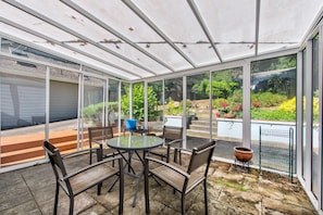 A covered patio with a glass enclosure, featuring a round table and chairs, a blue bowl, and a potted plant. - Stunning Sammamish Lake View Home near Weowna Park (Bellevue)