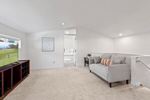 Amplia sala de estar con un televisor de pantalla plana grande, un sofá gris con almohadones decorativos, un mueble de entretenimiento de madera y una puerta que da a un balcón.