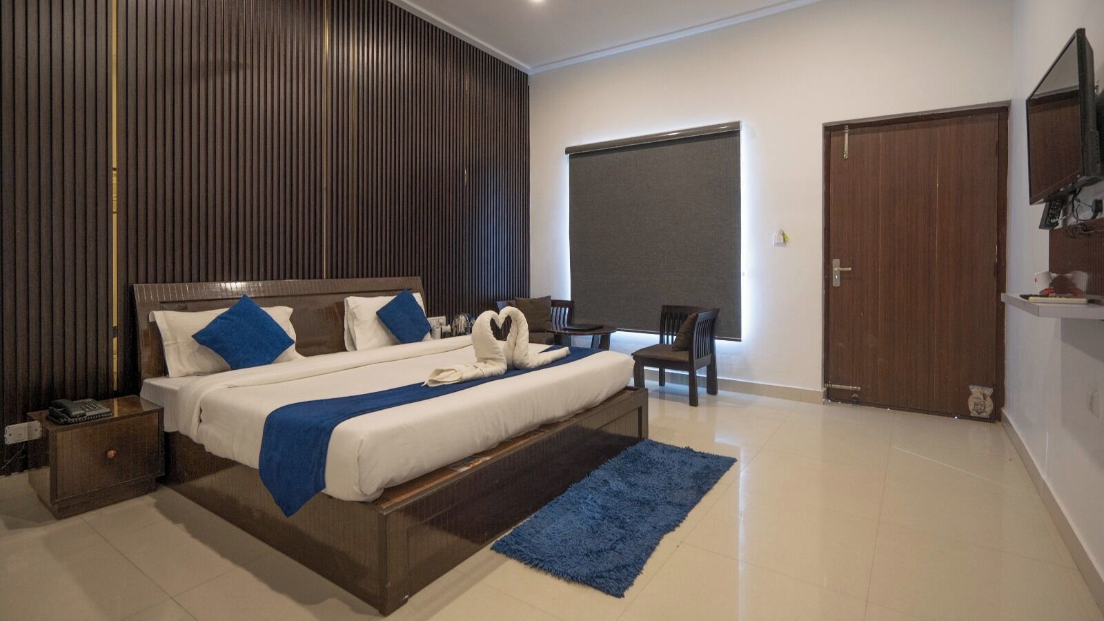 A modern hotel room with a large bed, a desk, a chair, and a wardrobe.