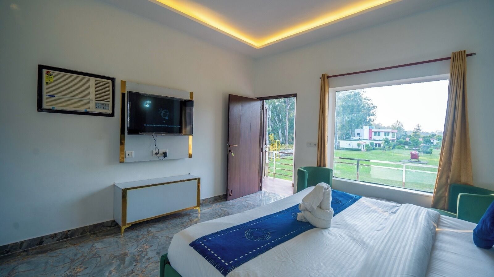 A hotel room with a bed, a TV mounted on the wall, a desk, and a view of the outdoors.