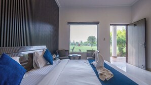 A hotel room with a large bed, a view of a golf course, a balcony, and a door leading outside. - Corbett Holiday Forest Resort (Belparao)