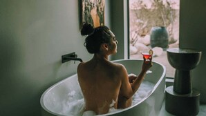 A person in a freestanding bathtub with a view of the outdoors through a window.