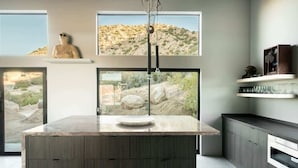 A modern kitchen with a central island, large windows with desert views, and minimalist decor.