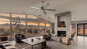 A spacious living room with a large window, leather sofas, a coffee table, and a fireplace.