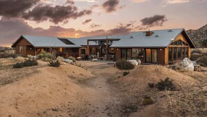 A modern desert-style building with a large patio area, multiple windows, and a prominent chimney.