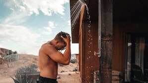 A man standing outside a building, with a showerhead above him.